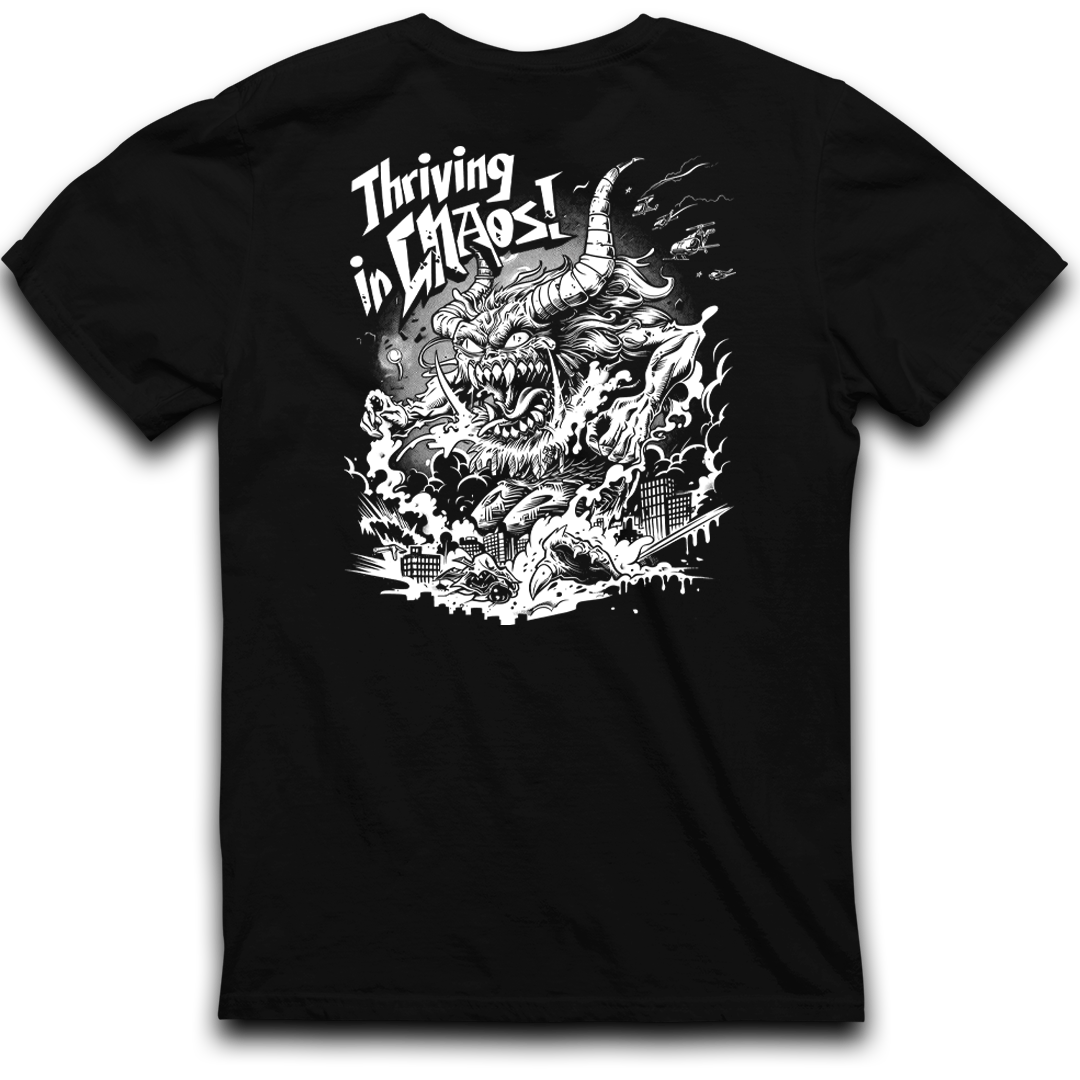 A CaliforniaScumbags Thriving In Chaos - Black Heavyweight Tee featuring a fierce, horned creature engulfed in flames, with buildings below being destroyed. The text above the creature reads, "Thriving in Chaos!" in a bold, dynamic font. The design is in white, creating a stark contrast against the shirt's boxy fit and black background.